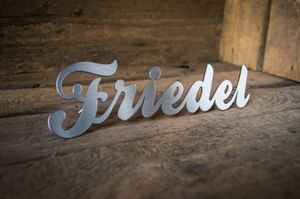 Schriftzug Friedel Schriftzug Friedel aus gebürstetem Edelstahl vor Holzwand